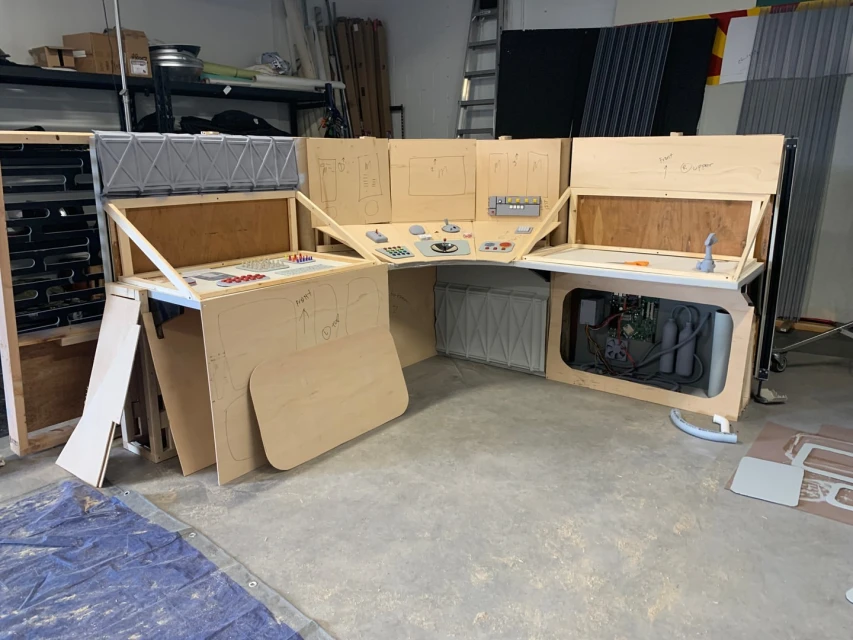 A fabricated spaceship control panel setup made of plywood, featuring sketches and various control elements in an indoor environment.